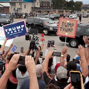 Tandis que le convoi présidentiel circule sur la rue, des dizaines de personnes se tiennent près du chemin, pancartes à la main.