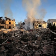 De la fumée s'échappe de deux maisons à moitié détruites par un missile, beaucoup de débris sont empilés devant les édifices.