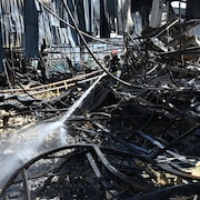 Un pompier arrose les décombres d'un magasin, où des morceaux de métal jonchent le sol.