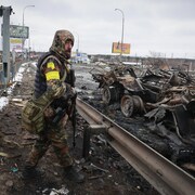 Un homme armé se tient près de véhicules brûlés.