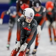 Une patineuse de vitesse, les mains sur les genoux, sourie après une course.