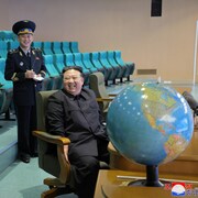Kim Jung-un se montre réjoui en compagnie de trois personnes, devant un globe terrestre.