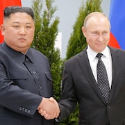 Côte à côte, les deux hommes se serrent la main en regardant droit devant eux. Seul Vladimir Poutine esquisse un sourire.