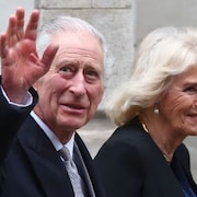 Le roi Charles III, souriant, salue des gens aux côtés de la reine Camilla.