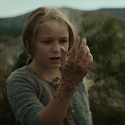 Photo promotionnelle du film La grande marée : une jeune fille apeurée regarde sa main, couverte d'abeilles. Derrière elle, un paysage montagneux et rural. 
