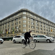 Des voitures et un cycliste roulent au centre-ville de Winnipeg, devant l'ancien bâtiment de la Baie d'Hudson.
