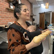 Léa St-Louis montre un pain à un client. Sa fille dort dans un porte-bébé ventral.