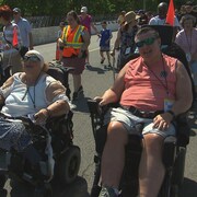 Des personnes circulent à pied et en fauteuil roulant sur une piste de course automobile. 