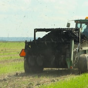 Un tracteur épand des boues dans un champ agricole.