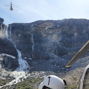 Un hélicoptère est au pied du glacier Bow du parc national Banff, alors qu'un autre vole dans le ciel.