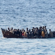 Une grosse barque à moteur pleine à craquer de migrants progresse sur l'eau.