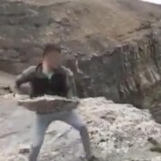 Image granuleuse, capture d'écran d'une vidéo, sur laquelle on voit un homme portant une grosse roche, qu'il s'apprête à lancer dans le vide.