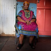 Ouma Katrina Esau, en tenue sud-africaine, assise sur une chaise.