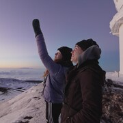 Deux personnes sur le haut d'une montagne, et une d'elles pointe au ciel.