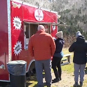 Des gens en rang devant un camion-restaurant rouge qui vend des sandwichs au homard.