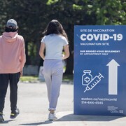 Un homme, un adolescent et une adolescente marchent près d'une pancarte annonçant un site de vaccination contre la COVID-19.
