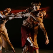 Trois danseurs professionnels sur une scène font des mouvements chorégraphiques. 
