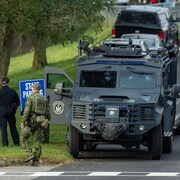 Des membres de forces de sécurité sont postés aux abords d'une rue et sur une pelouse à côté d'un véhicule blindé.