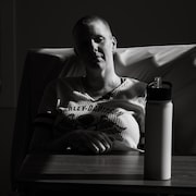 Caroline Lamontagne est dans son lit, derrière une table d'à point, sa bouteille d'eau posée dessus, en octobre 2022, à Edmonton, en Alberta.