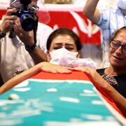Une femme portant un masque pleure au-dessus d'un cercueil recouvert du drapeau libanais.