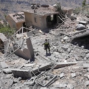Un employé en uniforme est posté dans un amoncellement de ruines et de maisons bombardées.