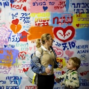 Une femme tient une bombe aérosol à côté d'un enfant devant un mur rempli de graffitis.