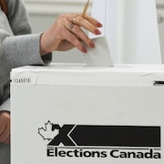 Une femme dépose un bulletin de vote dans une boîte ornée du logo d'Élections Canada.