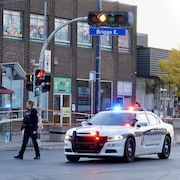 Une policière marche dans une rue commerciale à proximité de sa voiture de patrouille et d'un abribus.