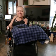 Une femme assise dans un fauteuil roulant électrique est entourée de plantes dans son appartement de Winnipeg.