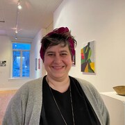 Une dame qui sourit dans une galerie d'art avec des tableaux accrochés au mur.