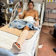 Lucas Arsenault dans un lit d'hôpital fait un signe de la main. 