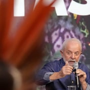 Le président Lula parle dans un micro devant une personne qui porte une coiffe.