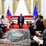 Nicolas Maduro, assis sur un fauteuil doré, est au centre de deux rangées de diplomates aussi assis dans une pièce du palais présidentiel de Caracas. Un drapeau du Venezuela et un de l'Union européenne sont accrochés.
