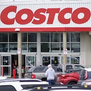 Un homme marche entre plusieurs voitures stationnées pour se rendre à l'entrée d'un magasin Costco.