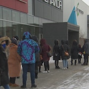 Des gens attendent dehors avant de rentrer dans un magasin.