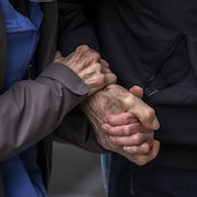 Une paire de mains d’une personne âgée s'agrippent à une autre main.