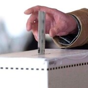 Une main dépose un bulletin de vote dans une boîte.