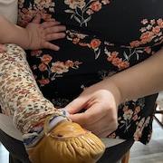 Un bambin qui porte un mocassin traditionnel en cuir est tenu par une femme enceinte sur sa hanche pendant qu'elle replace le petit pantalon de l'enfant. 