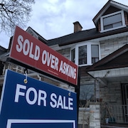 Une affiche de vente immobilière, sur laquelle on peut lire « Sold over asking » (« Vendu au-dessus du prix demandé »), devant des maisons en rangée.