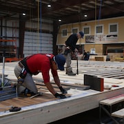 Des employés procèdent à l'installation du plancher d'une future maison préfabriquée.