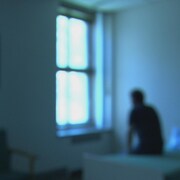 Un patient d'un hôpital psychiatrique assis sur un lit regardant par la fenêtre. 