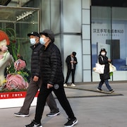 Des gens habillés en tenues hivernales marchent avec un masque sur le visage. 