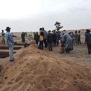 Plusieurs Maliens sont debout près de fosses creusées dans le sable.