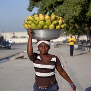Une vendeuse transporte un grand bol métallique remplis de plusieurs dizaines de mangues sur sa tête. Elle vend 5 fruits pour 2 dollars dans les rues de Port-au-Prince.
