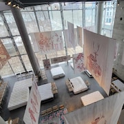 Œuvre composée d'une vingtaine de sérigraphies accrochées au plafond, sous lesquelles se trouvent des matelas et des chaises.
