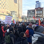 Plusieurs personnes se tiennent debout au centre-ville de Montréal, certaines brandissant des pancartes ou des drapeaux.