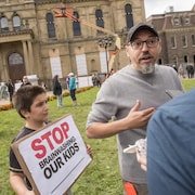Deux personnes discutent près d'un enfant tenant une pancarte sur laquelle il est écrit : « Arrêtez de laver le cerveau de nos enfants ».