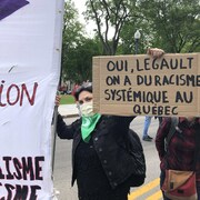Une femme tient une pancarte où on peut lire : « Oui, Legault, on a du racisme systémique au Québec », lors d'une manifestation devant l'Assemblée nationale. 