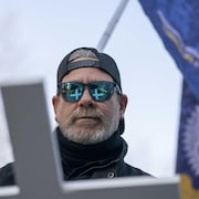 Un homme porte une croix blanche qui se reflète dans ses verres fumés.