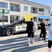 Des manifestants, dans une rue, près d'un véhicule de police.